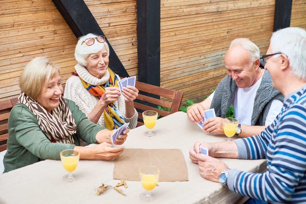 cheerful seniors playing card game at lunch table on outdoor terrace laughing happily at Willoughby Grange Care Home